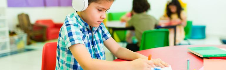 Child in headphones writing on A4 pad